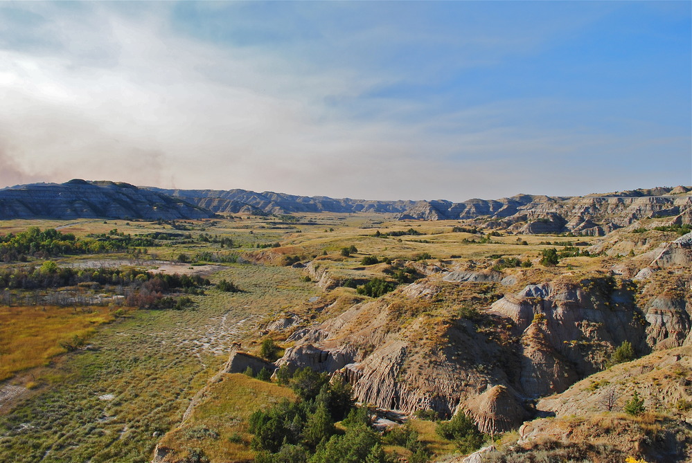 River valley of drying prairie vegetation and barren buttes line the horizon. 