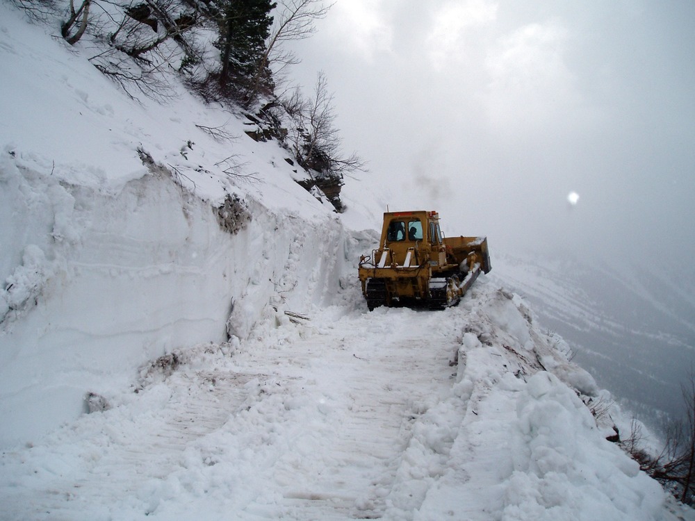 Bull dozer pushing snow over cliff on Going-to-the-Sun Road
