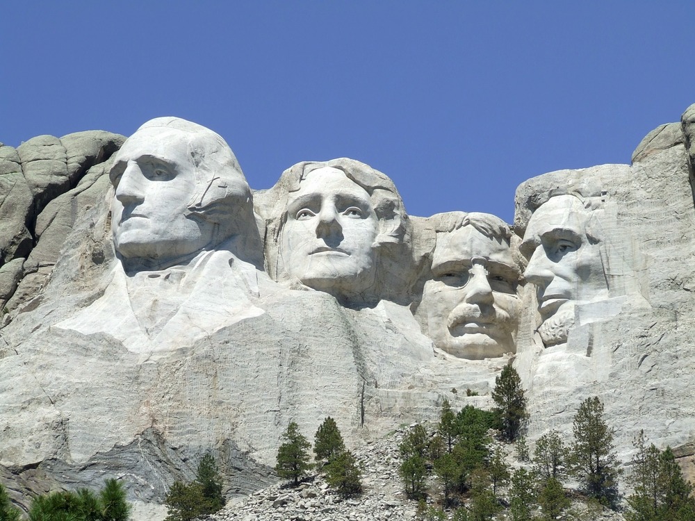 A full view of Mount Rushmore, taken from a view to the right of the mountain. Washington and Lincoln are seen from a side profile, where Roosevelt and Jefferson are seen straight on.