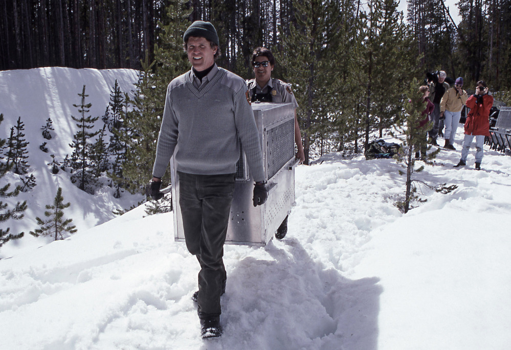 Two men carrying a metal crate on a snow covered trail.