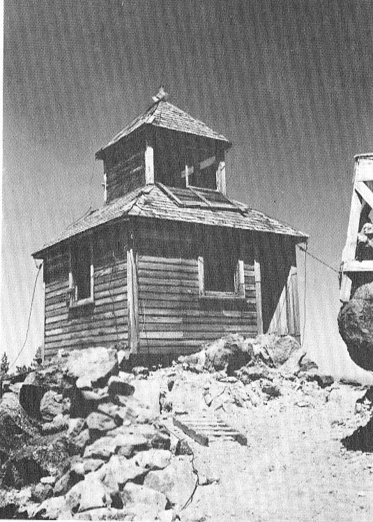 A wooden-sided, cupola style fire tower stands on a rocky landscape.