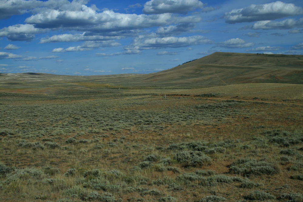 A wide grassy and sagebrush covered valley with a sloping hill on the right side, and clouds overhanging.