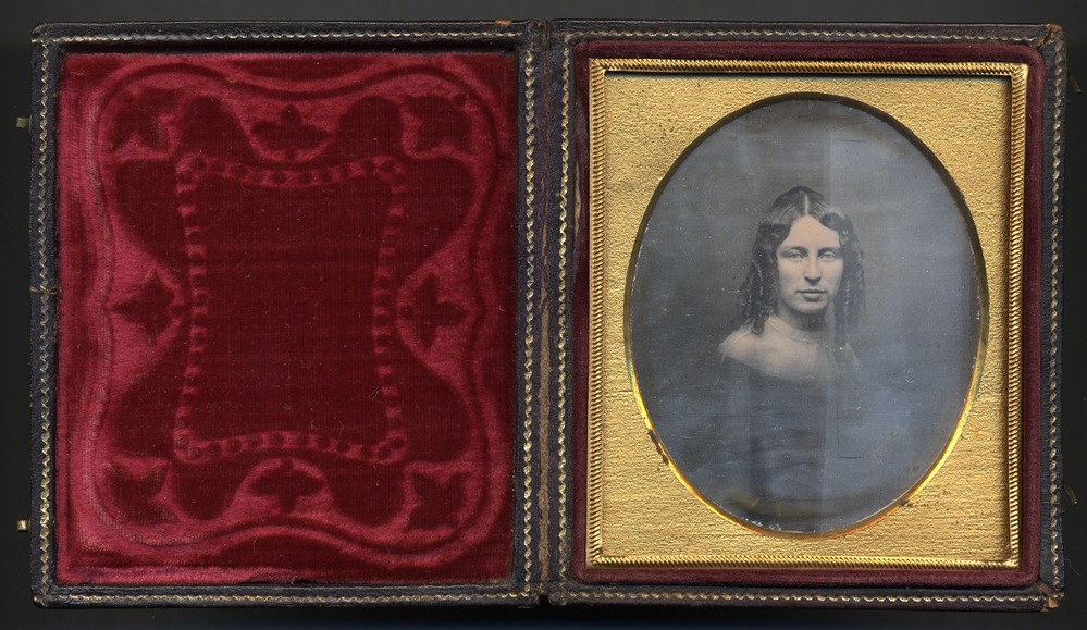 Daguerreotype of young woman with corkscrew curls in case with red velvet lining and oval frame.
