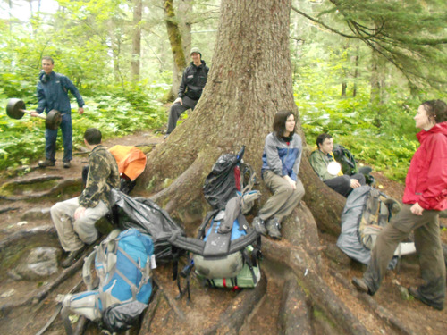 People with backpacking gear gather around the base of a tree.