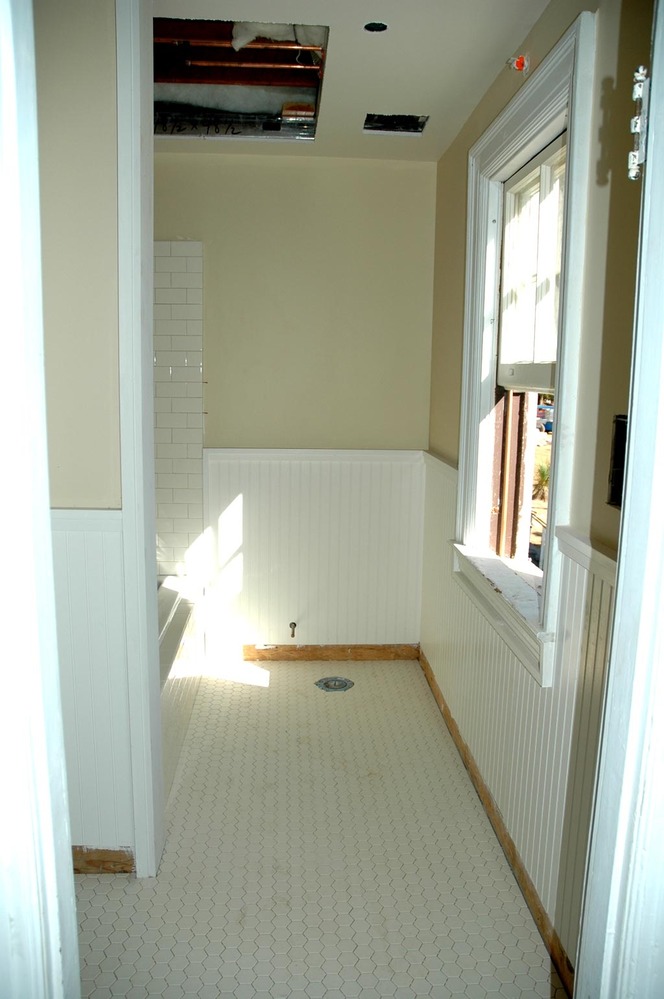 This photo shows a new finished bathroom with hexagonal floor tiles and wooden wainscotting.