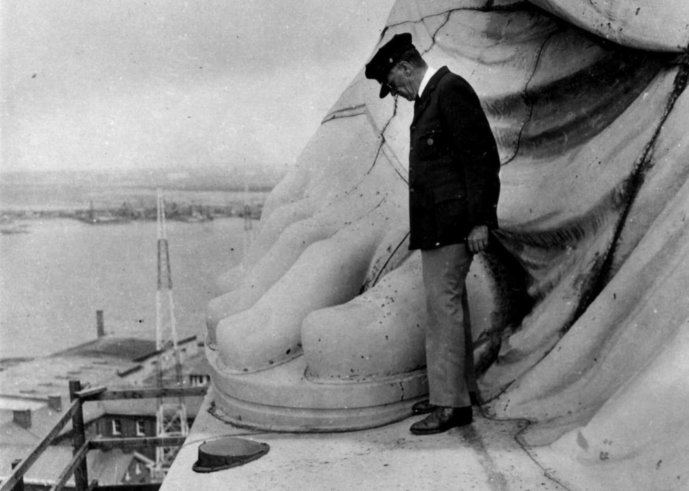 Superintendent O. Camp standing at Statue's foot where her symbolic broken shackle and chains are located. circa 1930's