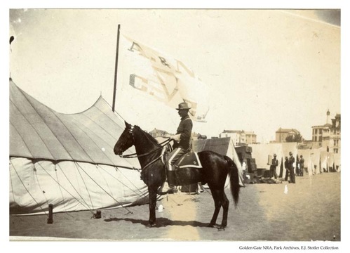 “Major John Hauwe of 2nd battalion, Camp Merritt, Cal. July 1898.” Man sitting on horse with flag in background.