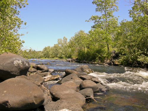    A river flows over boulders and remnants of a dam.