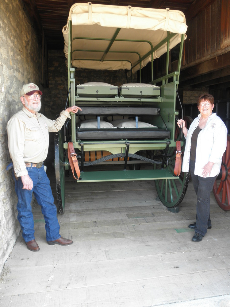 Don and Connie Werner pose inside stone carriage house with green covered wagon