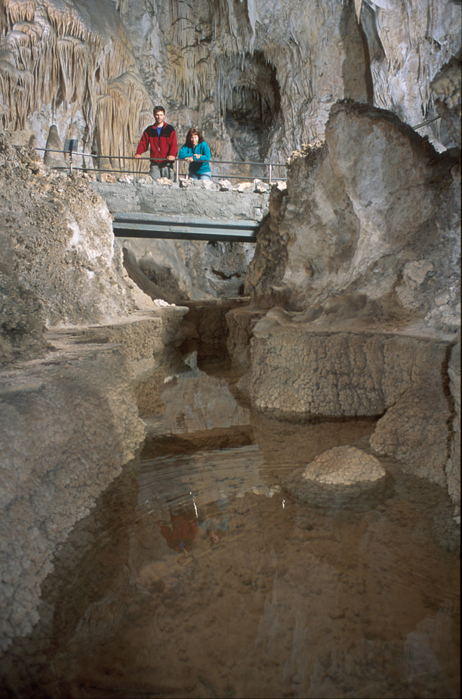 Visitors stand on a bridge over a large cave pool.