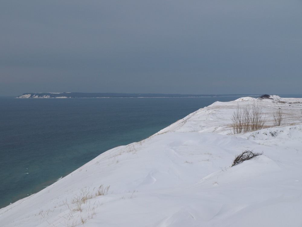 The view of South Manitou Island covered with snow on the horizon and the top of Sleeping Bear Dunes on the right in the winter gives an impression of a stark environment, but it is home to a wide variety of animals and plants that become active in spring.