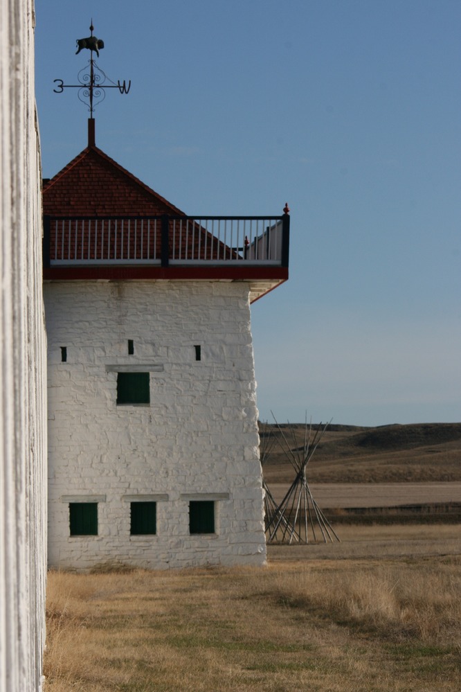 The red-roofed northeast bastion with wood-pole tepee frames and hills in the background.