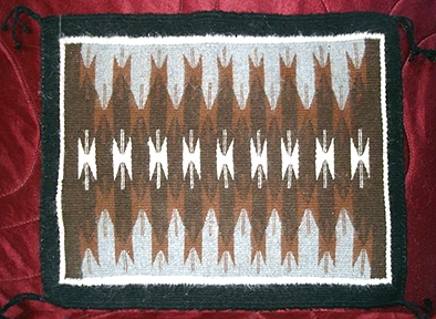Navajo rug, VanWinkle Butterfly design. All colors may be used. The VanWinkle butterfly design is an hourglass shape, sometimes with short lines radiating out perpendicularly from where the two triangle points meet. Usually without a border.