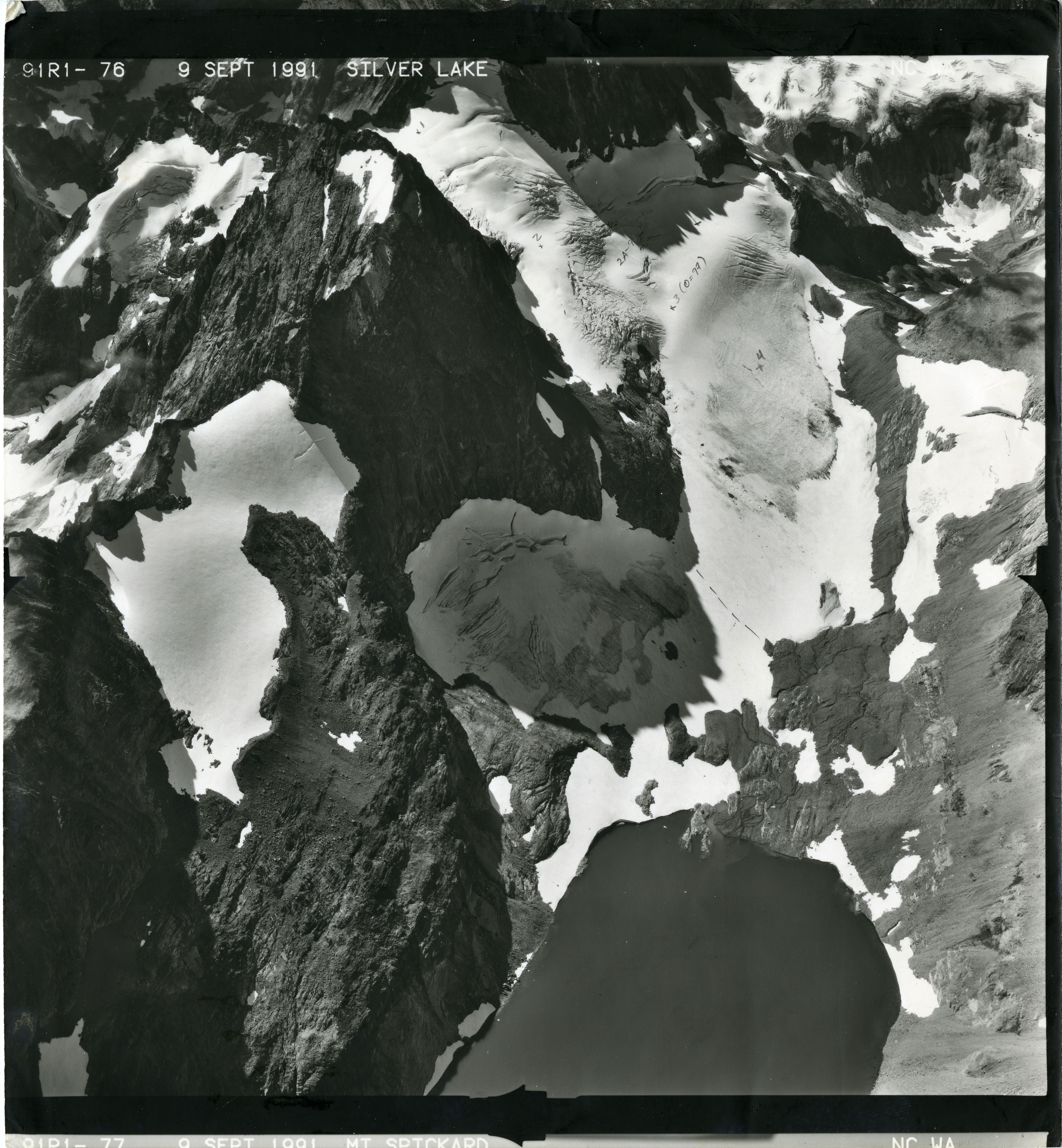 Black and white aerial photograph of glacier, snowfields and alpine lake on mountain peak.
