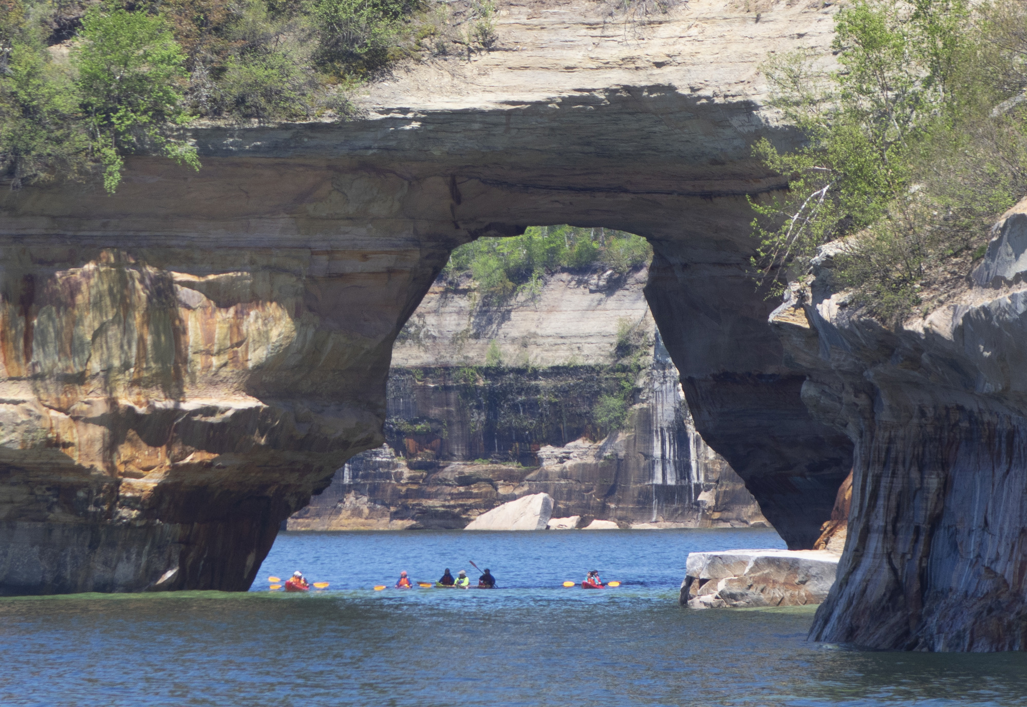 Kayakers are paddling under a rock arch.