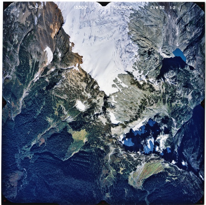 Color aerial photograph of glaciated mountain peak with forested valleys below.
