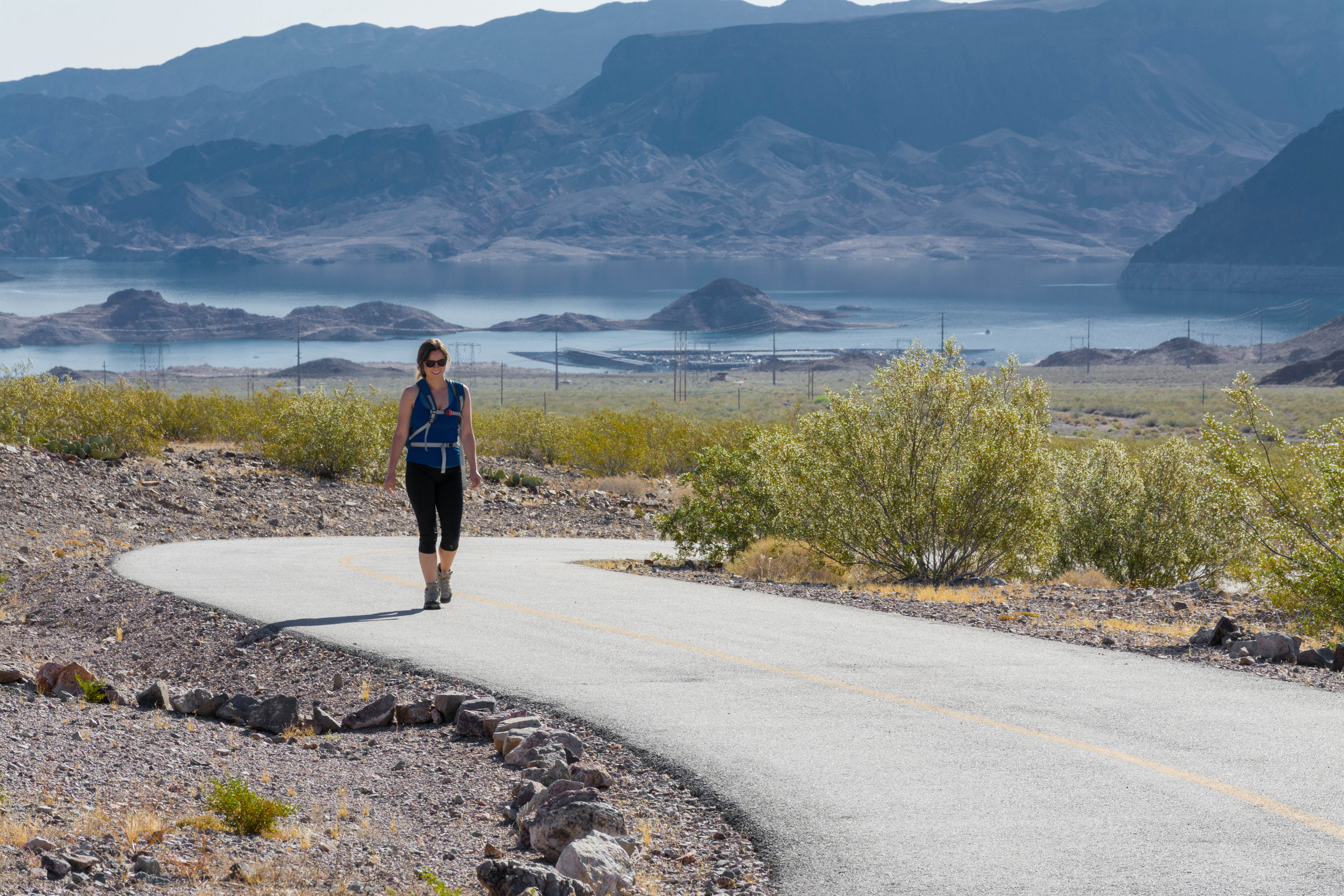 Hiker on S curve of paved trail, lake and mountains in background 