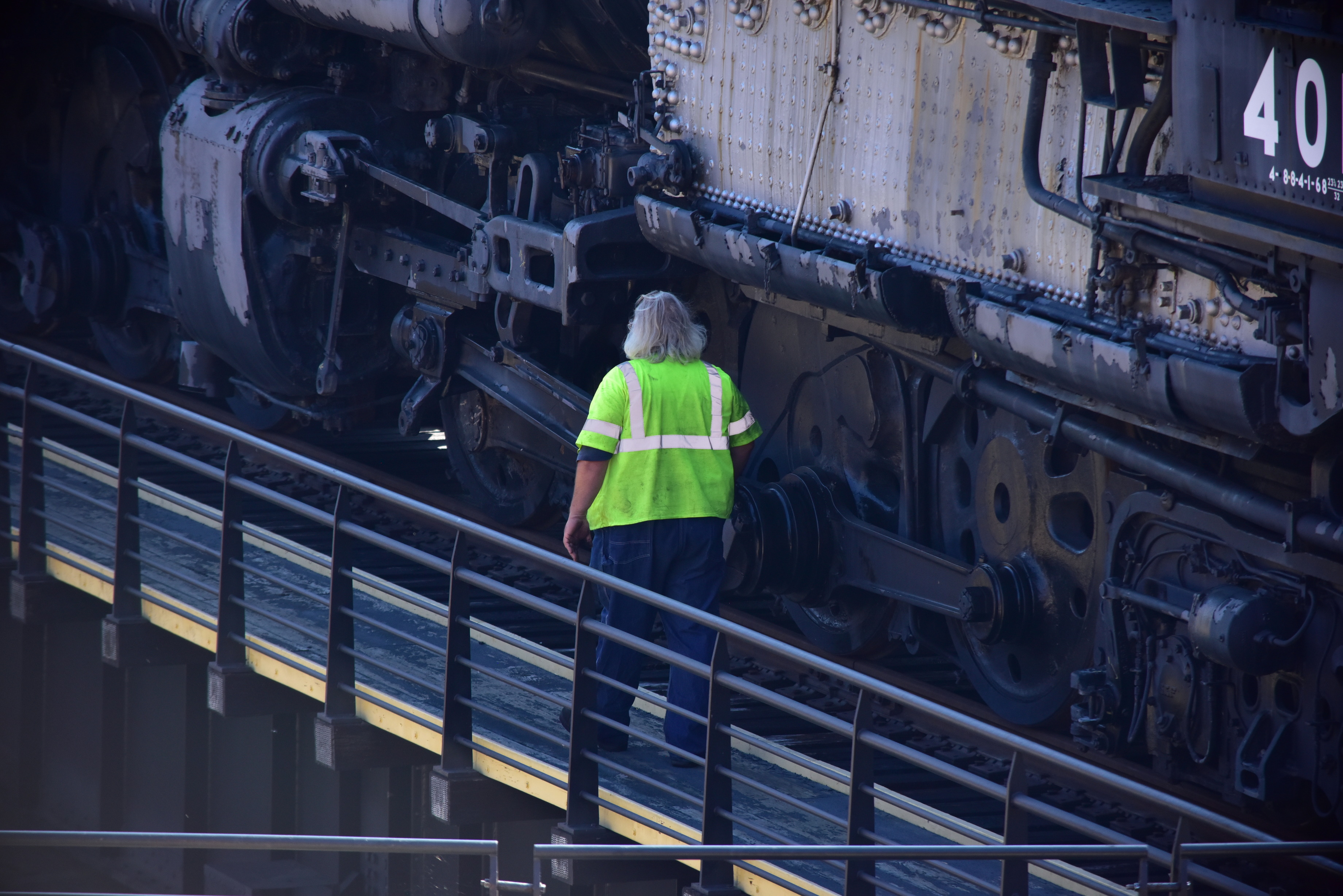 A lone employee in high visibility gear walking next to a large train as it rests on the turntable for inspection
