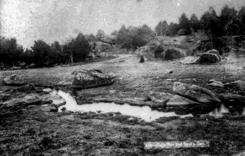 This black and white 1880s William Tipton photograph shows Devil’s Den from northeast of the famous boulders. Two rock formations jutting up from the earth can be seen in the center of the photograph. No roads or monumentation exists in the area and heavy tree growth can be seen all around the Den area.