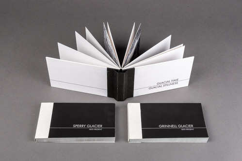 Two handmade books, "Sperry Glacier: 1850-Present" and "Grinnell Glacier: 1850-Present" lie face up next to each other. The handmade book, "Glacial Time, Glacial Stillness" is propped up behind them with the spin of the book facing the camera.