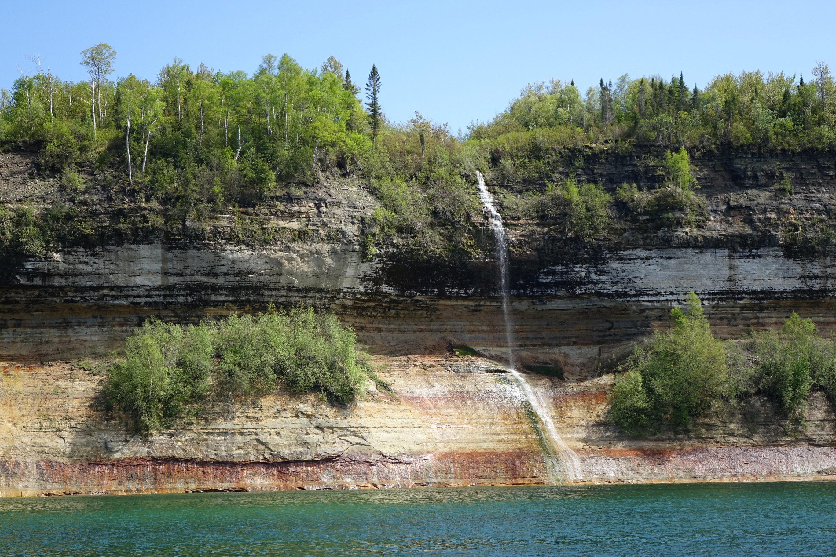 A narrow stream of water flows over the eroded cliffs and into Lake Superior