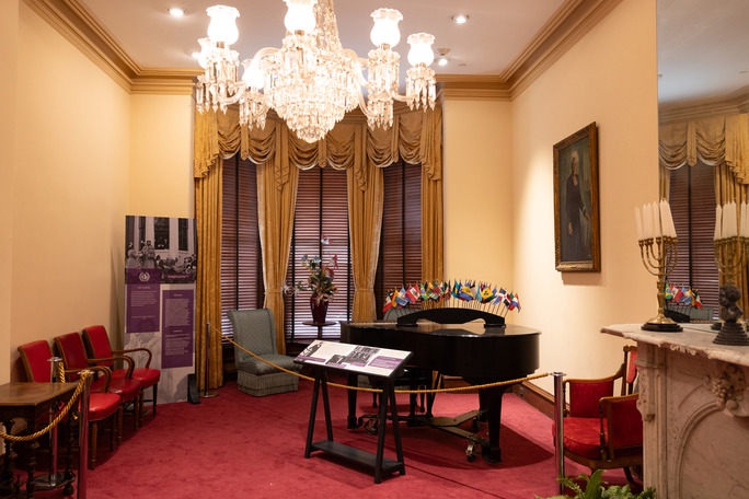 A room with a grand piano, and a chandelier in a historic building. 