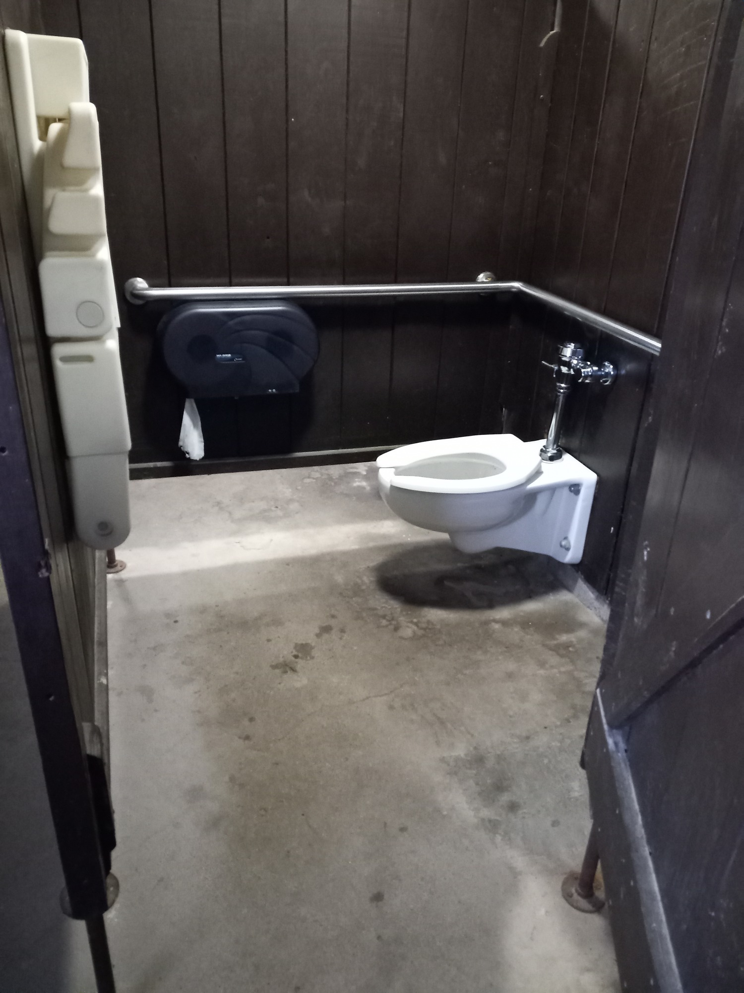 Restroom has cement floors and stalls with gaps at the bottom of the rustic privacy walls. 