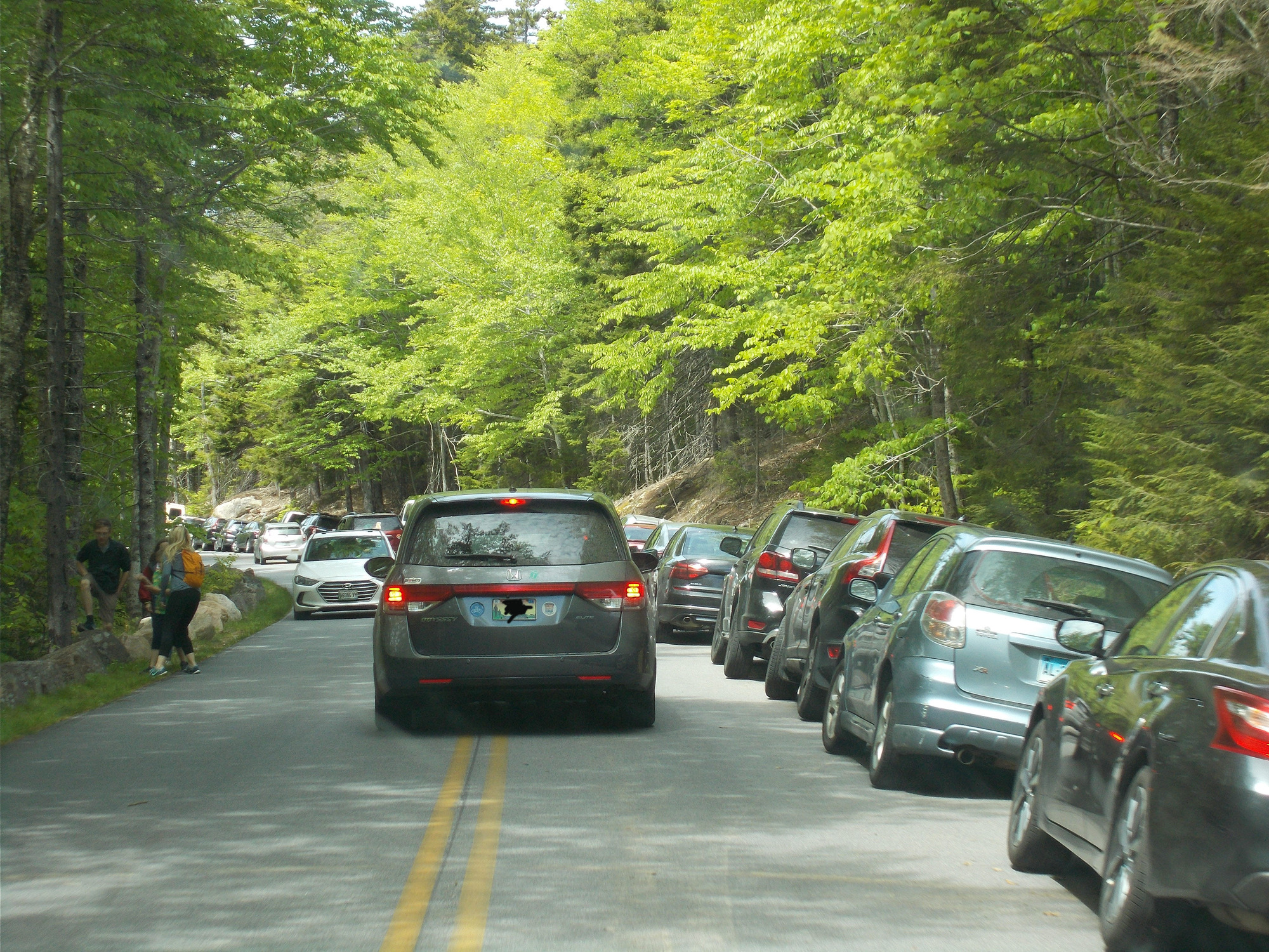 a blue mini van crosses the yellow line in the center of the road due to cars parked on the right side of the road