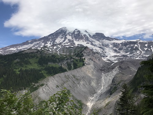 A glacier carves down a mountain into a deep valley, with a river spawning from the terminus of the glacier. 
