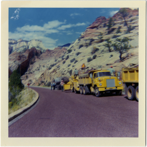 Road construction vehicles lined up on side of road during chipsealing.
