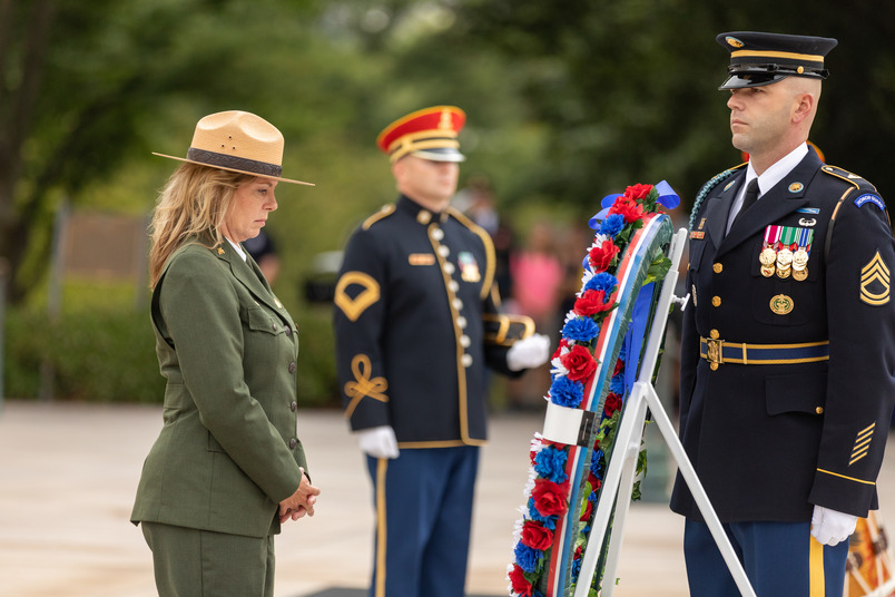 Director Kym Hall, in her dress uniform, stares solemnly at a red, white and blue wreath that she just placed in front of the tomb. Two soldiers in uniform stand guard near her.
