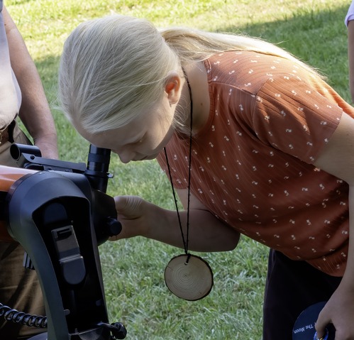 A young girl looks through the lens of a telescope during the day. 