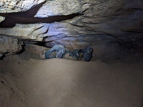 View of two cavers' feet and legs as they crawl into tight passageway. 