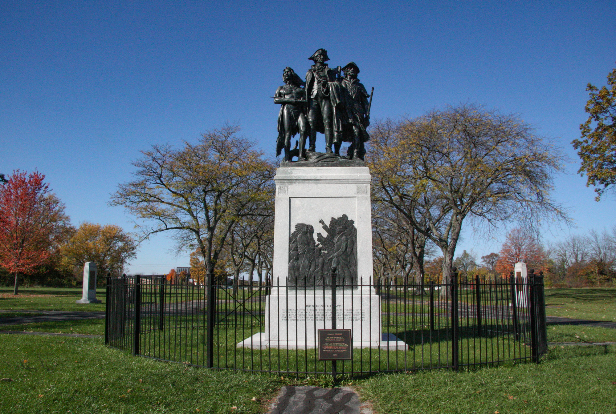Statue of a Native American, soldier, and frontiersman encircled by a fence in a park
