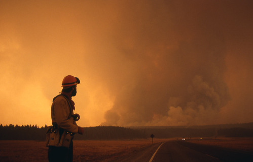 Fire fighter looking over shoulder at orange sky and smoke