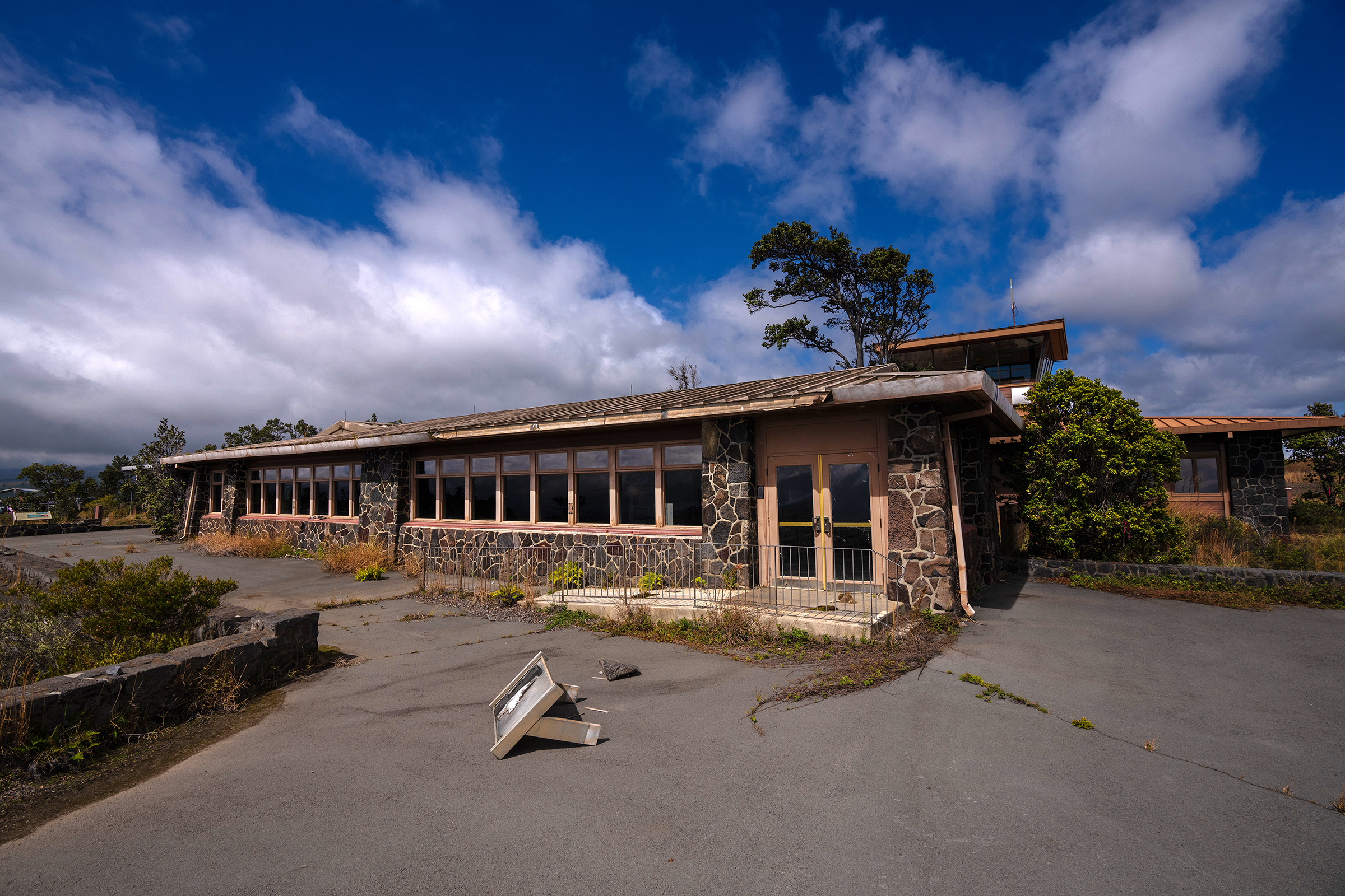A broken exhibit sign laying on its side on a concrete slab outside a one-story building with a rock facacde 