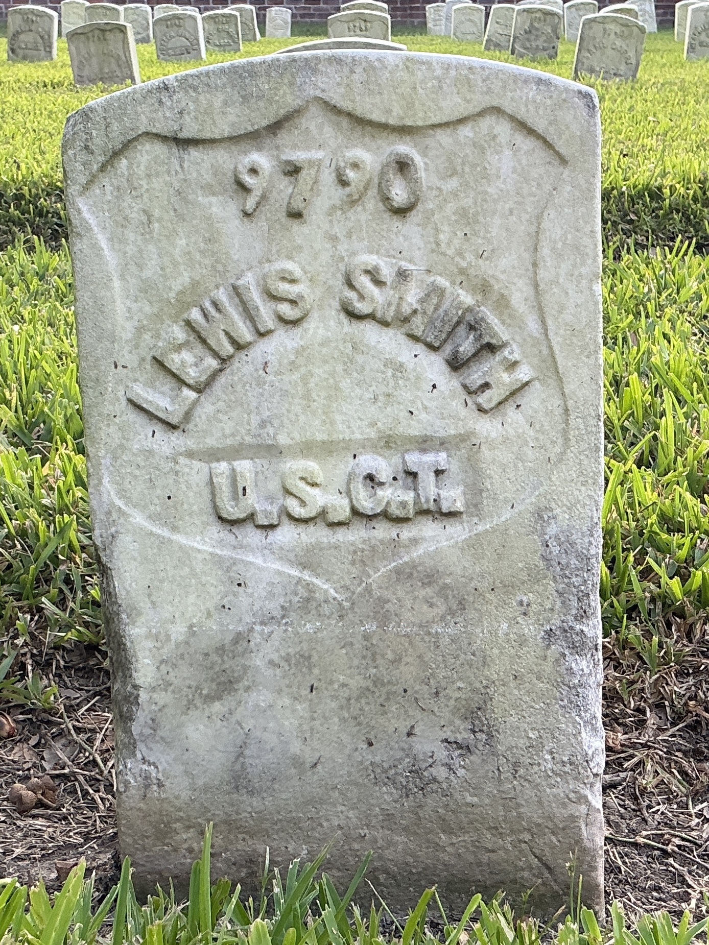Front of historic upright marble headstone with recessed shield with recessed lettering face.
