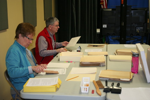 Two individuals use brushes to delicately remove dust and debris from the documents.