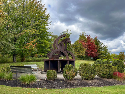 Metal memorial made of elevated semi-circles, or broken Olympic rings, situated in a garden plaza