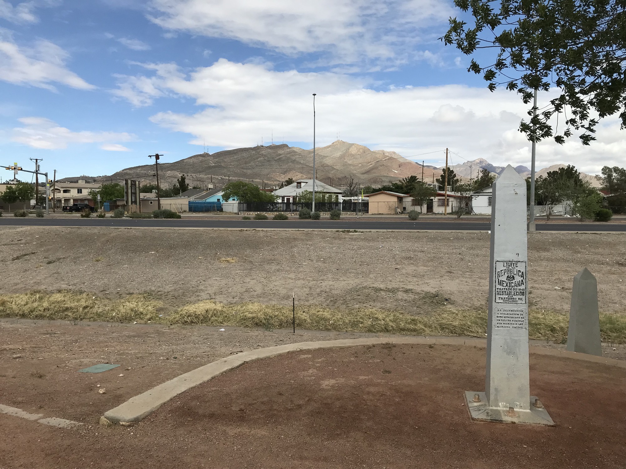 A sign in front of a dirt road with mountains in the background.