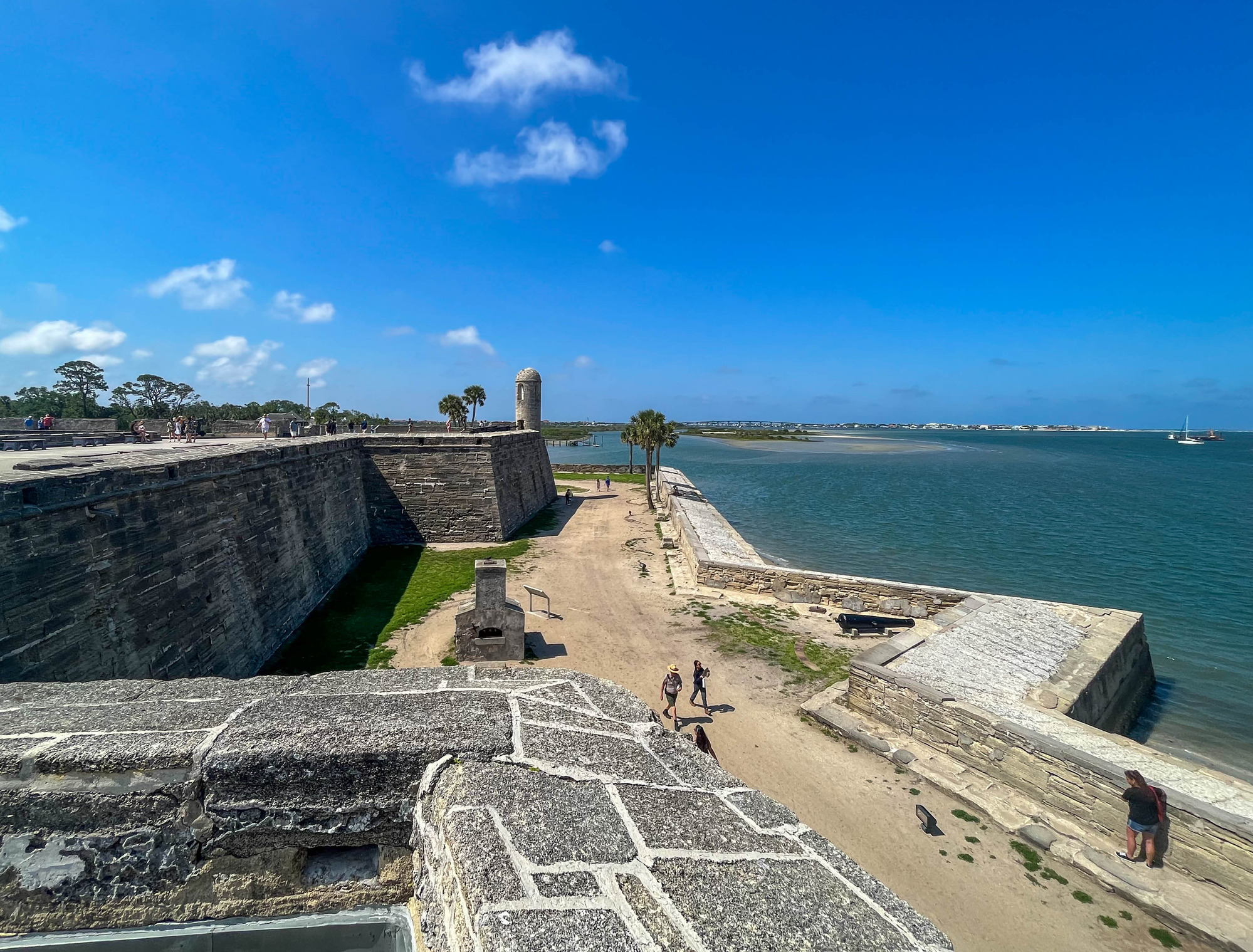 Aerial view of people walking in between a historic fort and a bay 