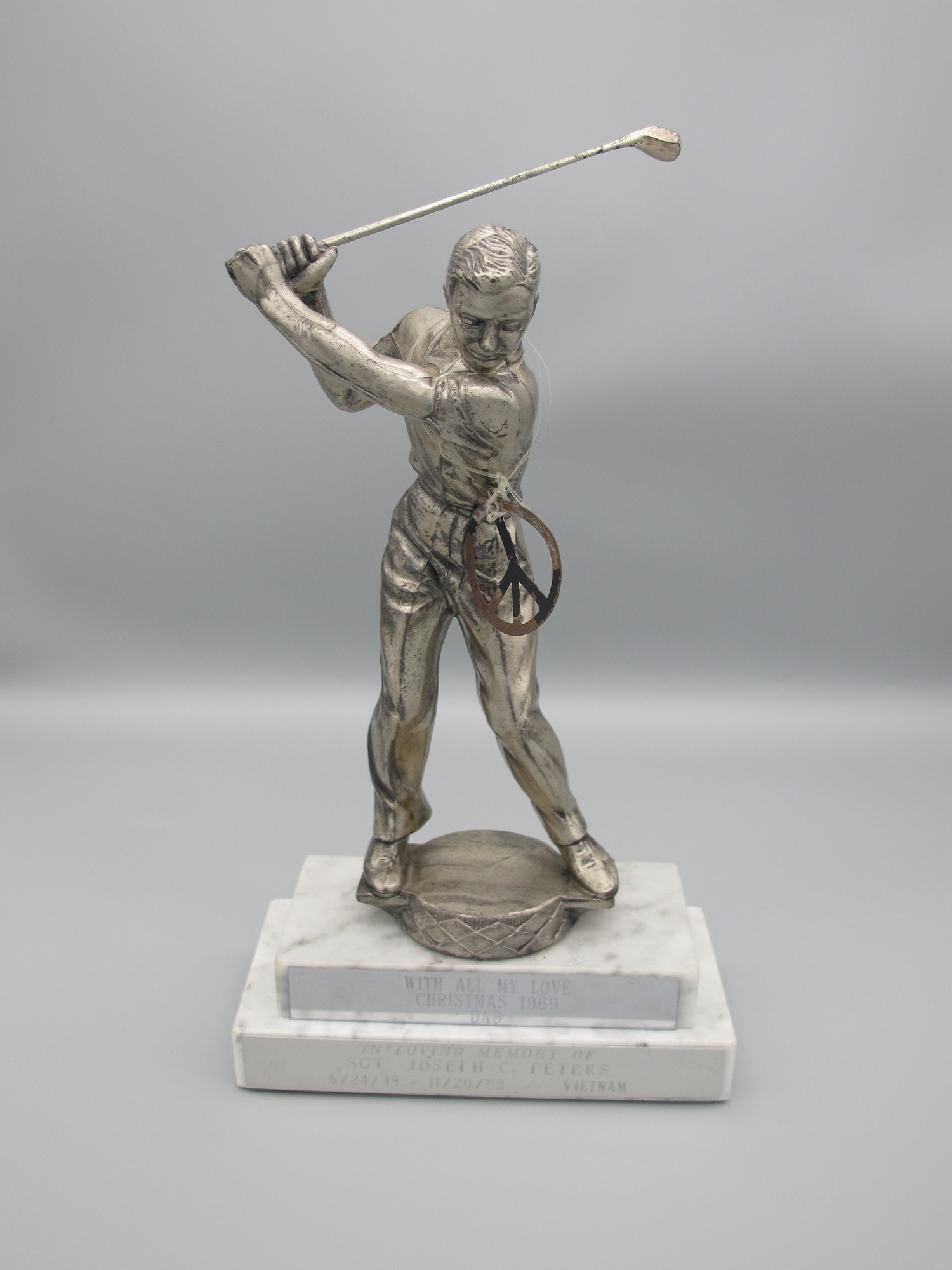 Trophy of a male figure holding a golf club in mid-swing. Figure is standing on a two-tiered marble base. Inscribed plates on the base say "In Loving Memory of Sgt. Joseph C. Peters, 6/24/49 - 11/20/69, Vietnam" and "With All My Love, Christmas, 1969, Dad".