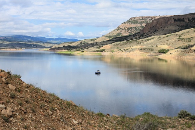A large body of water with surrounding mesas. One boat is floating in the middle of the water.