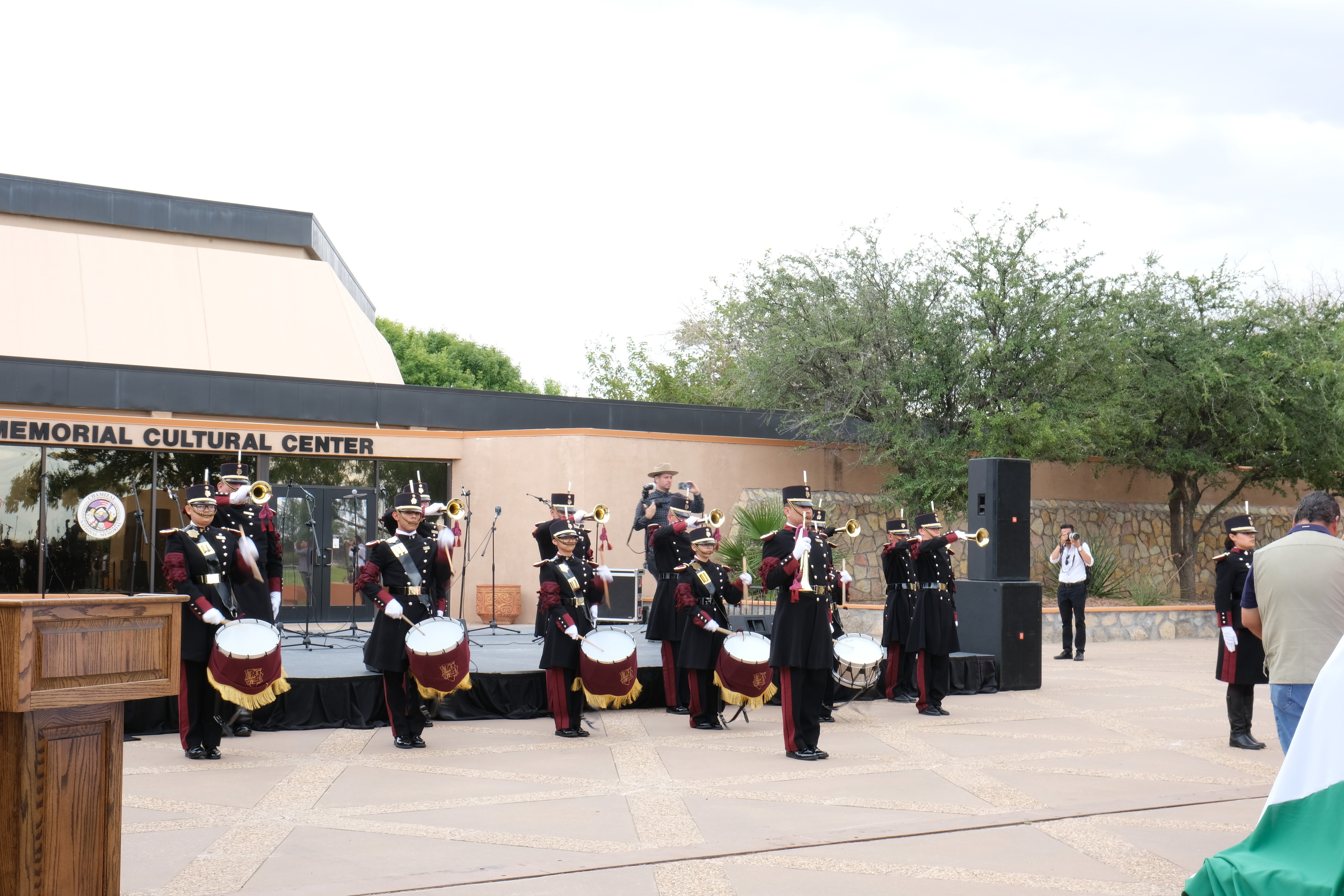 A dozen people in black and maroon band uniforms play trumpets and drums