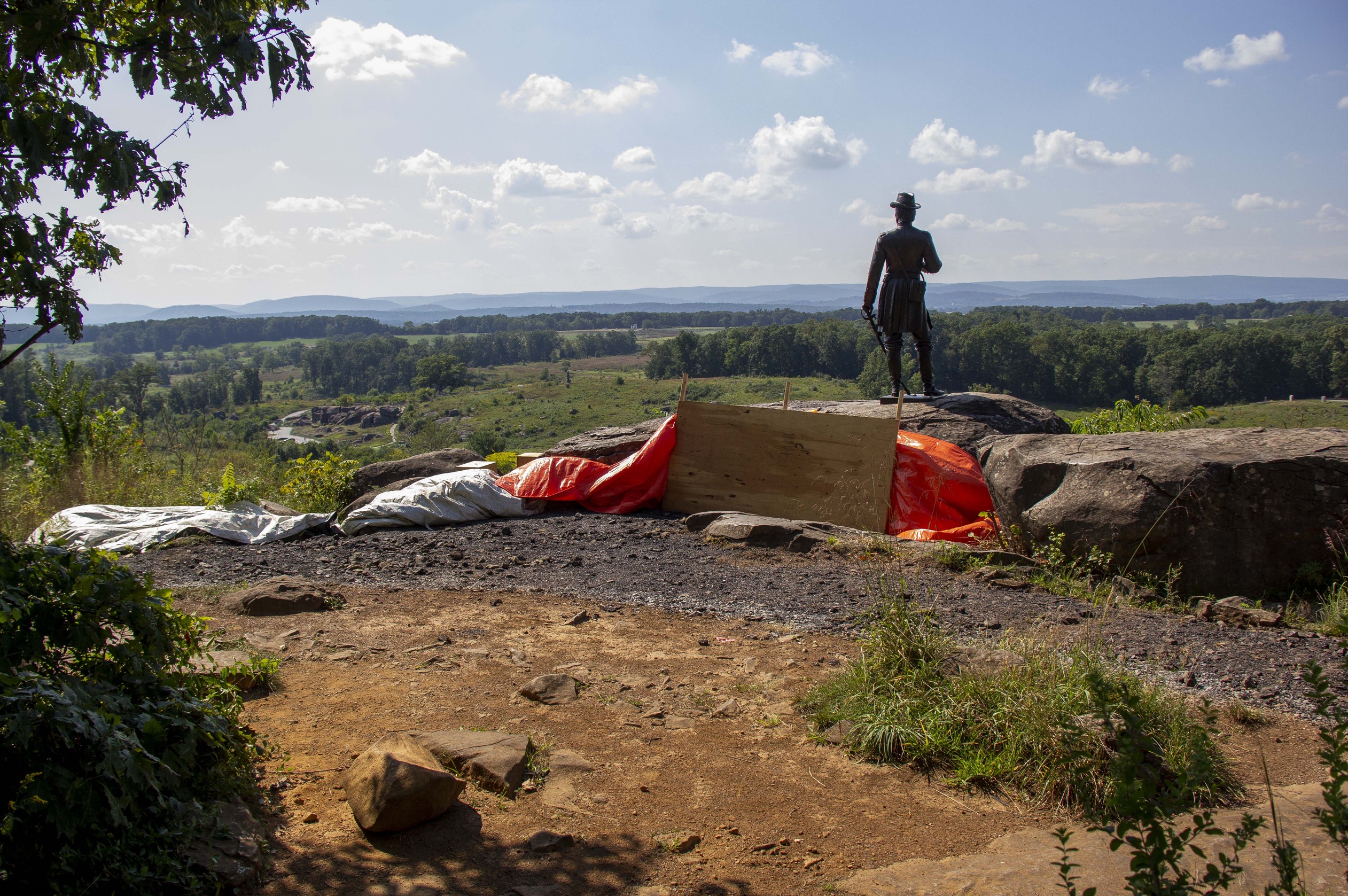 A statue of a man on the edge of a hill is silhouetted against a bright daytime sky.