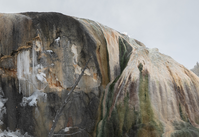 A mound of travertine has water bubbling up on the right side and icicles on the left.