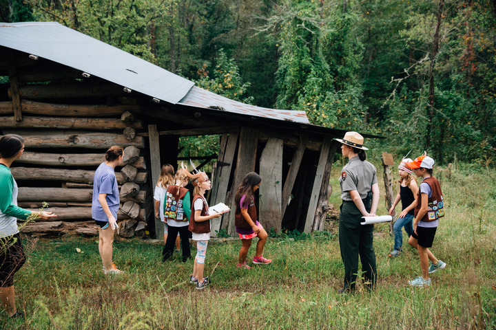 A ranger leads a group of children around the outside of a log structure on the Beaver Jim Villines Farmstead in Ponca