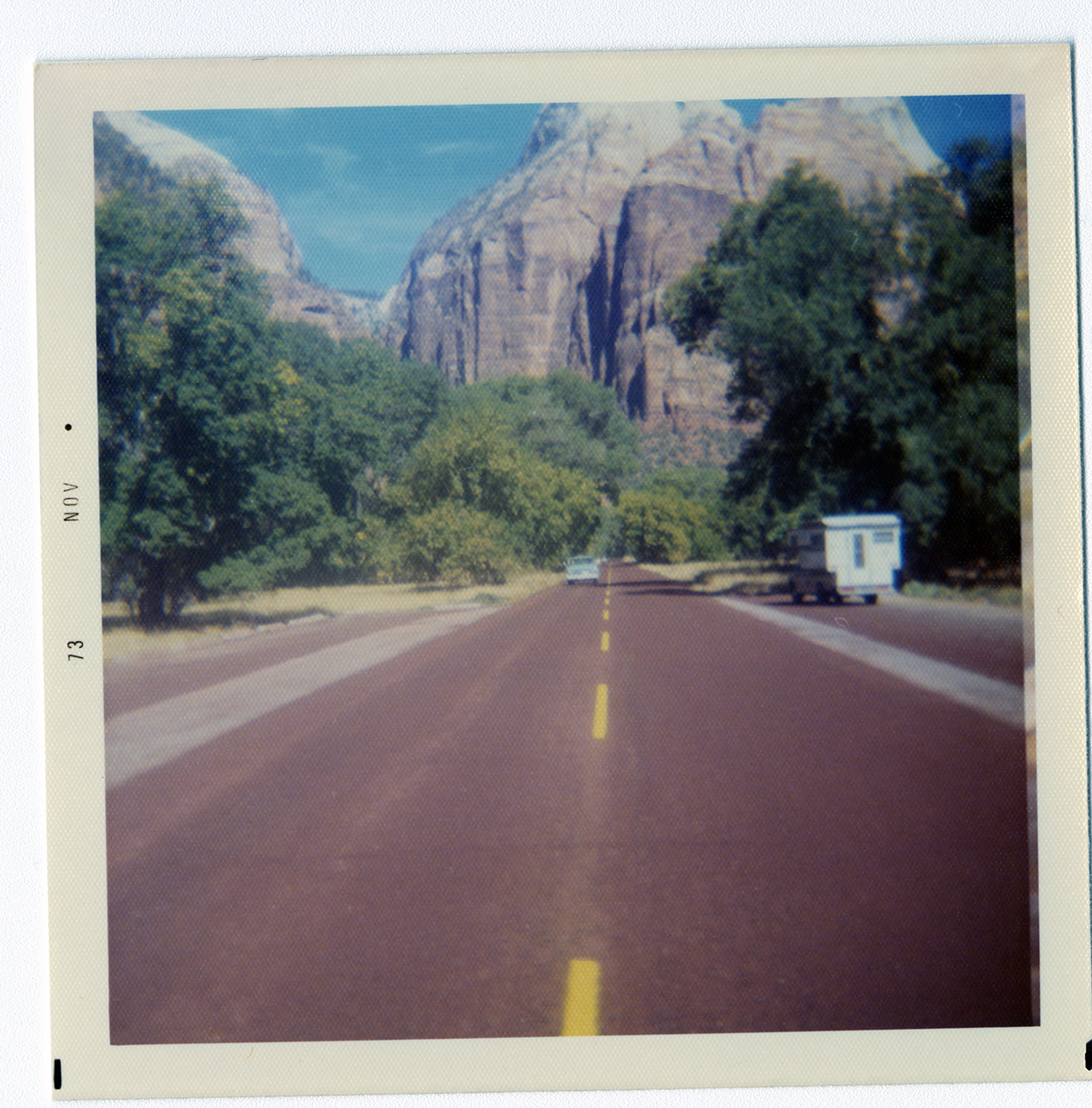 Two-way road divided by yellow dotted lines with Zion landscape in background.