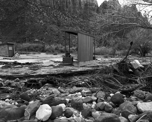 The December 6, 1966 flood damage - near Watchman amphitheater. Debris, boulders, damaged truck are visible after the water receded.