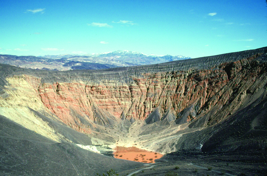 A large crater of red and black rock under a blue sky.